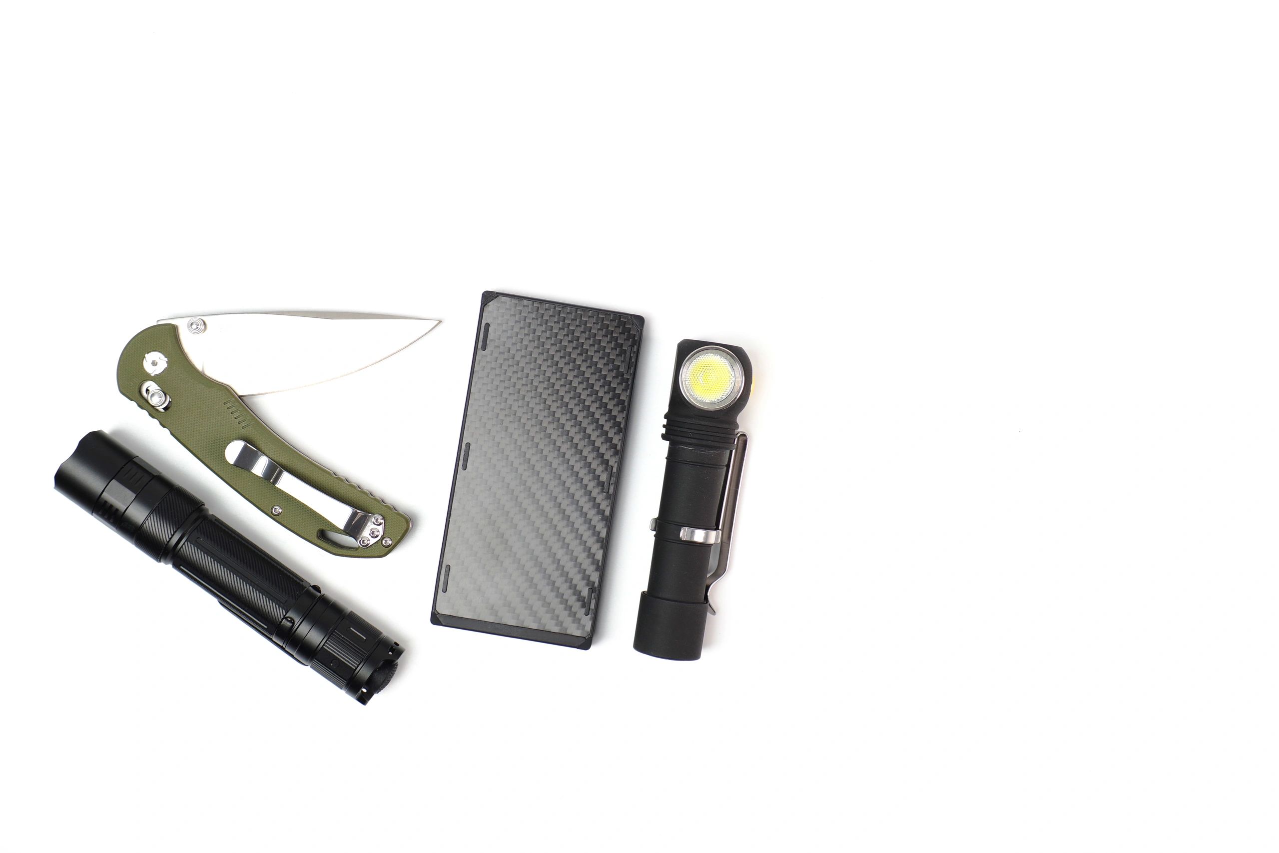 Pocket flashlight, folding knife, and power bank arranged in a minimal studio setup